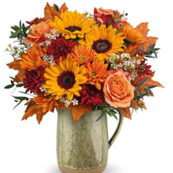 Autumn bouquet of sunflowers, roses, and mums in a ceramic pitcher