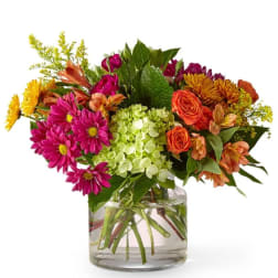 Mixed bouquet of pink, orange, and yellow flowers in a clear glass vase