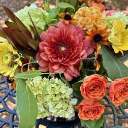 Mixed bouquet with a large pink dahlia, orange roses, and pale green hydrangeas