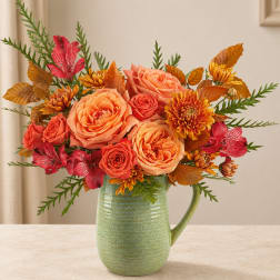 Orange and coral flowers arranged in a green ceramic pitcher