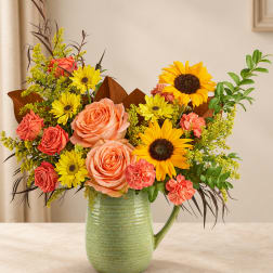 Bouquet of peach roses, sunflowers, and yellow daisies in a green pitcher vase
