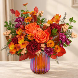 Orange roses and mixed fall flowers in a colorful glass vase