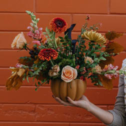 Mixed floral arrangement in a pumpkin-shaped vase held by a person