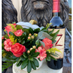 Pink rose and carnation arrangement beside a wine bottle