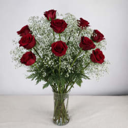 Red roses arranged in a clear glass vase with white filler flowers
