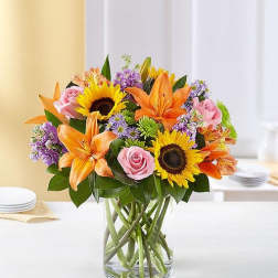Bouquet of sunflowers, orange lilies, and pink roses in a glass vase
