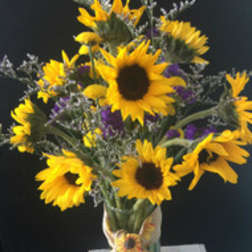 Bouquet of yellow sunflowers with purple accents in a clear vase