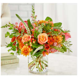 Mixed bouquet of peach roses and orange blooms in a clear glass vase