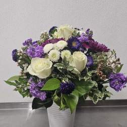 White roses and purple mixed flowers arranged in a white ceramic vase