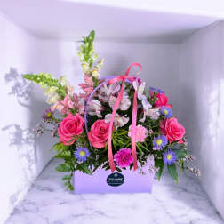 Pink roses and mixed flowers arranged in a lavender gift box with ribbon.