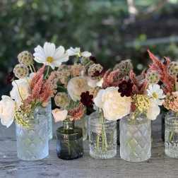 Small mixed flower arrangements in assorted glass bottles on a table