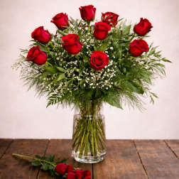 Red roses arranged in a clear glass vase with a single rose on the table