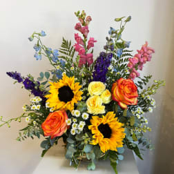 Colorful mixed bouquet with sunflowers, roses, and tall blue and pink blooms in a vase