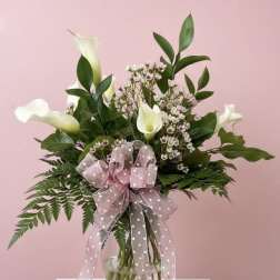 White calla lilies in a glass vase with a pink polka-dot bow