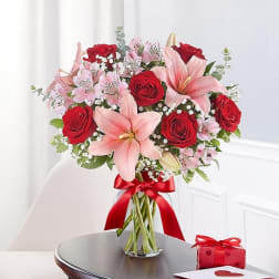 Bouquet of red roses and pink lilies in a glass vase with a red ribbon