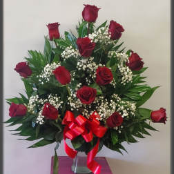 Red roses arranged in a clear vase with baby's breath and a red ribbon