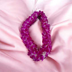 Purple orchid flower lei arranged in an oval shape on soft pink fabric