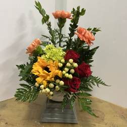 Mixed bouquet with red roses, yellow sunflowers, and peach carnations in a white vase