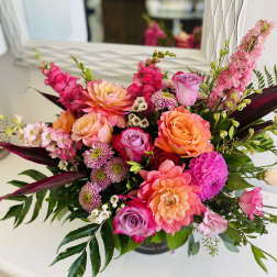 Bright arrangement of pink and orange dahlias, roses, snapdragons, and mums in a low glass vase