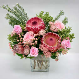 Bouquet of pink protea and roses with filler flowers in a clear glass cube vase