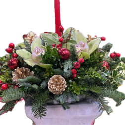 Holiday floral arrangement with red berries, orchids, and pinecones in a container