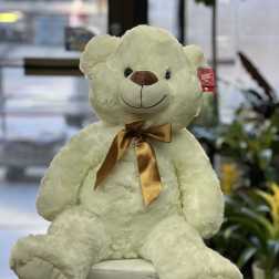 Cream teddy bear with a gold ribbon sitting on a pedestal