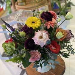 Mixed bouquet in a white vase with bright yellow, pink, red, and purple blooms
