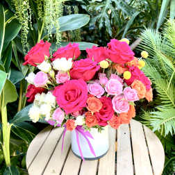 Bright mixed roses arranged in a white hatbox with a pink ribbon