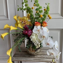 Tall mixed floral arrangement with yellow calla lilies, orchids, and roses in a metallic vase