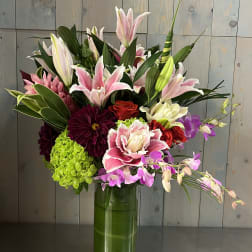 Mixed bouquet of lilies, orchids, roses, and hydrangeas in a glass vase