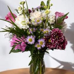 Mixed bouquet of white, pink, and purple flowers in a clear glass vase