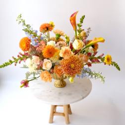 Colorful mixed flower arrangement in a gold vase on a round table