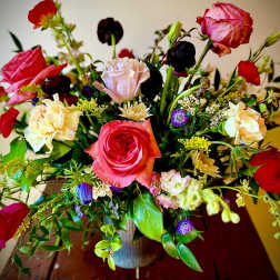 Vibrant mixed bouquet of pink and red roses with assorted blooms in a ribbed vase on a wooden table.