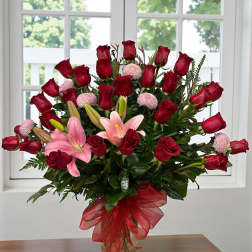 Bouquet of red roses and pink lilies in a glass vase with a red ribbon