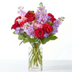 Bouquet of red roses, pink flowers, and purple blooms in a clear glass vase