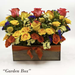 Mixed roses and small filler flowers arranged in a wooden box with an orange ribbon.