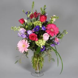 Mixed bouquet of pink, purple, and red flowers in a clear glass vase