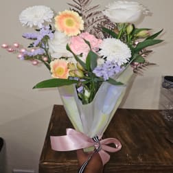 Bouquet of mixed pastel flowers wrapped in translucent paper with a pink ribbon