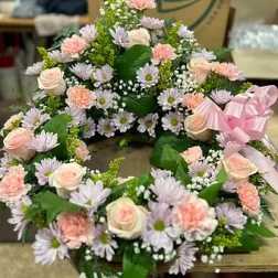 Pastel floral wreath with roses, daisies, and carnations on a pink ribbon
