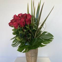 Red roses in a tall gold vase with tropical leaves