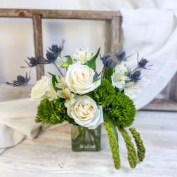 White roses and small white flowers in a glass vase with green accents