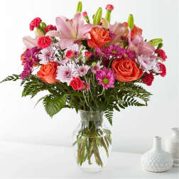 Mixed bouquet of pink lilies, roses, and daisies in a glass vase