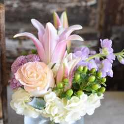 Pink lilies and roses arranged in a glass vase with white blooms