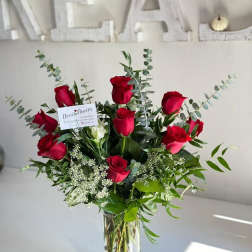 Red roses arranged in a clear glass vase with greenery