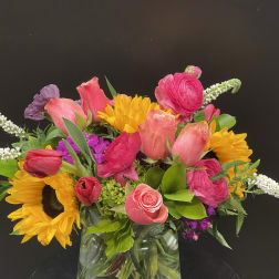 Colorful mixed bouquet with sunflowers, pink roses, and tulips in a glass vase