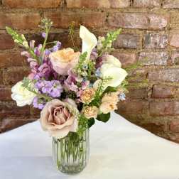 Pastel bouquet of roses, calla lilies, and purple blooms in a glass vase