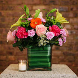 Mixed bouquet in a green glass vase with a small candle beside it