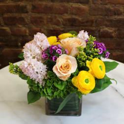 Mixed bouquet in a square glass vase with peach roses and yellow ranunculus