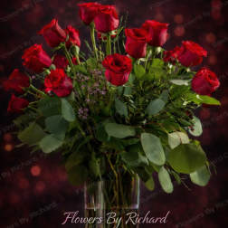 Red roses arranged in a clear glass vase with greenery