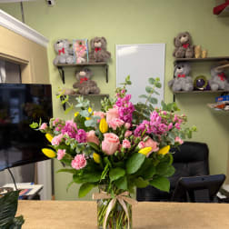 Pink and yellow flower arrangement in a glass vase with ribbon